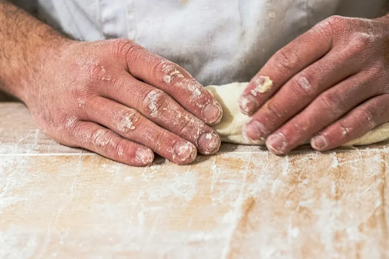 Des mains farinées façonnent un pâton sur le plan de travail